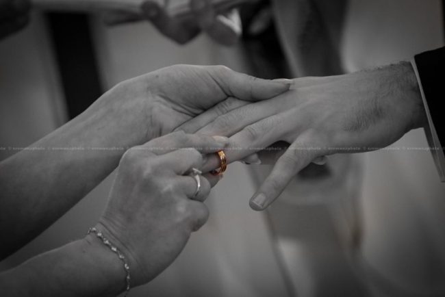 black and white picture of the ring being placed into the groom's finger, during the wedding vows